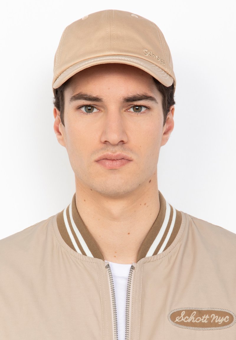 Beige Kappe mit runder Krone und einem steifen, gebogenen Schild. Mit tonalem Stich und dem Markennamen, der auf der Vorderseite gestickt ist.