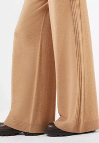 Hellbraune, weit geschnittene Hosen aus weichem Stoff, mit gerippten Bündchen und Seitenschlitzen, kombiniert mit dunkelbraunen, klobigen Schuhen.