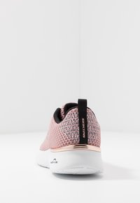 Rosa nätträningsskor med svart inredning, vit sula och roséguldkant vid hälen. Dragtab med logotyp på baksidan för enkel påtagning.