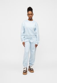 Φόρμα σε ανοιχτό γαλάζιο χρώμα με φαρδιά εφαρμογή, κατασκευασμένη από μαλακό ύφασμα, με ριμπ μανσέτες και ελαστική μέση με κορδόνι.