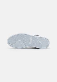 White rubber shoe sole with herringbone pattern, featuring textured areas and branding detail. Smooth finish with curved contours.