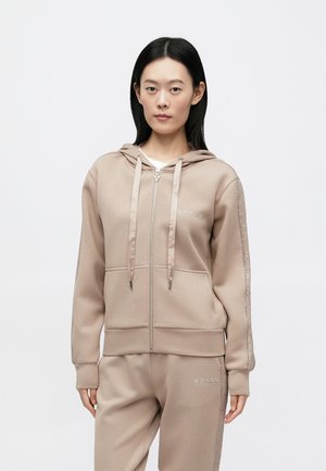 Sudadera con capucha beige con cremallera y cordones, confeccionada en material suave. Presenta un logo y detalles de acento en las mangas. Combina con pantalones a juego.