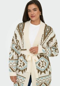 Ženska nosi bež, modro in rjavo vzorčasto jopico, zvezano v pasu, preko bele srajce, z zlatimi obročastimi uhani in prstani.