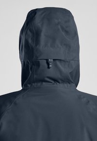 Veste imperméable gris foncé avec une capuche ajustée, mettant en avant un tissu lisse, un régulateur arrière et des détails de coutures subtils.