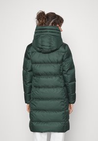Donkergroene pufferjas met een capuchon, voorzien van horizontale stitching en een middellange snit. Glad, glanzend materiaal met een zachte textuur.