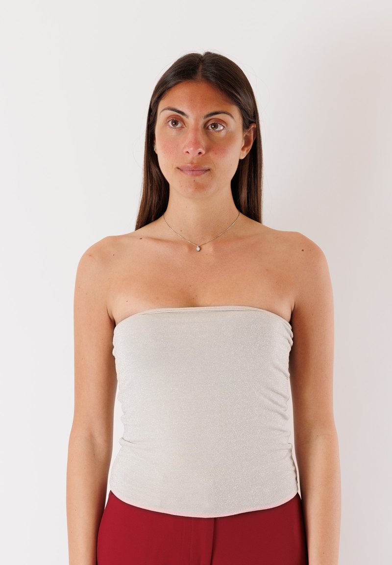Top senza spalline grigio chiaro con una texture traslucida e scintillante, design aderente e fascia elastica. Indossato con pantaloni rossi, esposto su uno sfondo neutro.