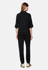 Schwarzes Jersey-Loungewear-Set mit einem subtilen Zebra-Muster. Das Oberteil hat eine lockere Passform mit 3/4-Ärmeln, kombiniert mit passenden, schmal zulaufenden Hosen und weißen Sneakers.