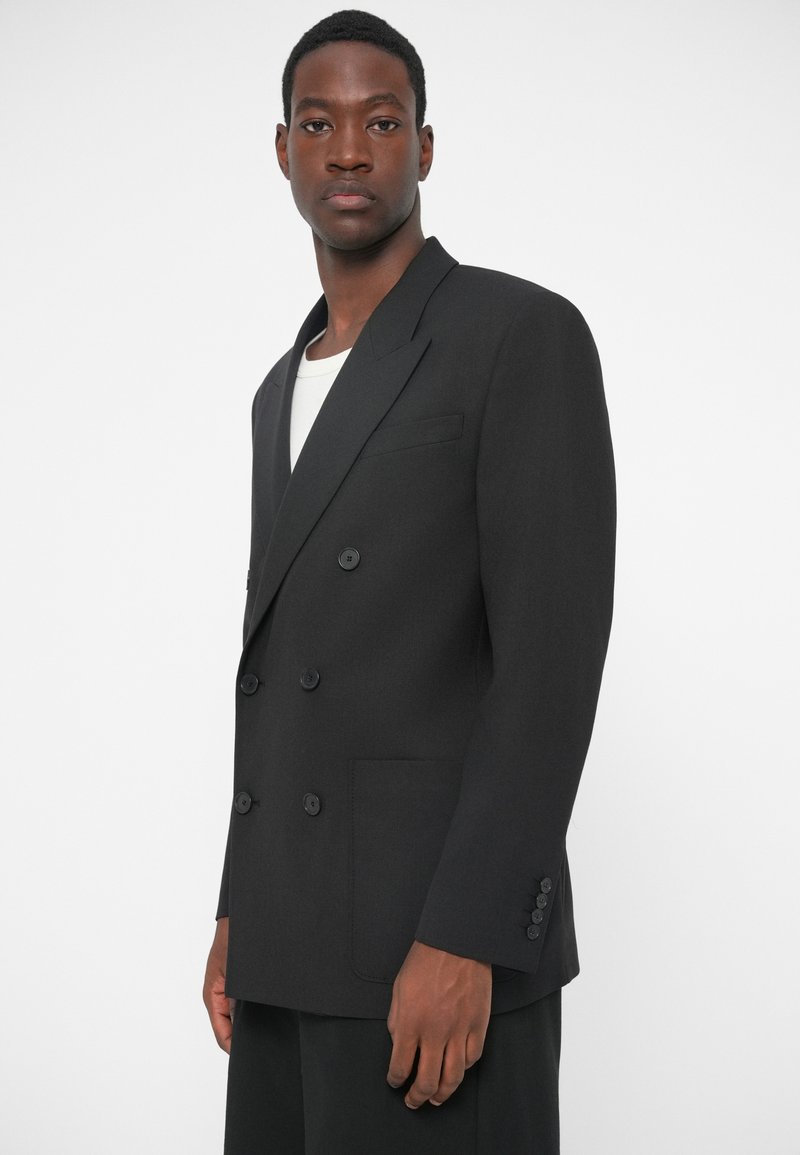 Sort dobbeltradet blazer med klapkrave, to forlommer og seks knapper. Lavet af tekstureret stof, har skræddersyet design.