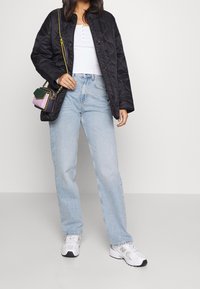 Černá prošívaná bunda přes bílý přiléhavý top, doplněná světle modrými džíny s rovnými nohavicemi a bílými teniskami. Malá vícebarevná kabelka.