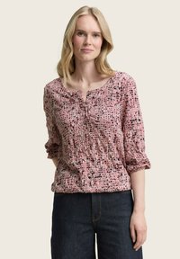 Rosa, strukturierte Bluse mit Rundhalsausschnitt und drei Viertel-Ärmeln, die ein buntes, abstraktes Muster in Schwarz- und Mauve-Tönen aufweist.