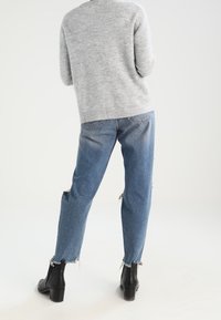 Maglione grigio a maglia abbinato a jeans chiari strappati e stivali alla caviglia neri, con orlo sfrangiato e tessuto testurizzato.