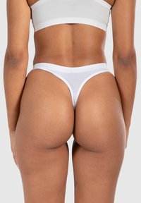 Tanga blanc avec une fine ceinture, en matériau élastique, présentant une texture lisse et une couverture minimale.