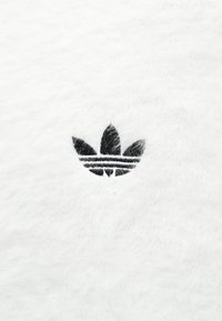 Tela blanca con un logo negro de tres hojas y tres rayas horizontales abajo. La textura parece suave y esponjosa.
