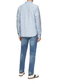 Jasnoniebieska koszula zapinana na guziki, z długimi rękawami, z miękkiego materiału, zestawiona z wyblakłymi niebieskimi dżinsami i białymi trampkami z czarnymi akcentami.