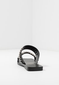 Svart platt sandal med en slät läderfinish, prydd med en vriden kedja längs den övre remmen och en minimalistisk design.