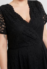 Svart spetsklänning med djup V-ringning, korta spetsärmar och en utsvängd kjol. Texturen är intrikat med ett blommönster.