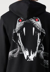 Sweat à capuche noir avec un grand graphisme d’une bouche de serpent ouverte montrant des crocs et des yeux rouges imprimés au dos.