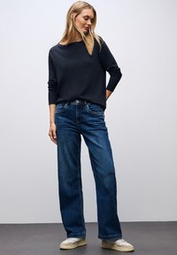 Marineblauer Langarmpullover kombiniert mit weiten, dunkelblauen Jeans und hellen Sneakers. Weicher Stoff, lockere Passform und eine dezente gerippte Textur.