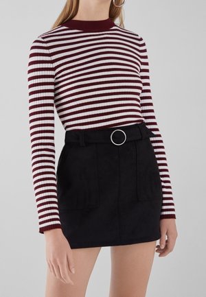 Mujer que lleva una camiseta de manga larga a rayas en granate y blanco metida en una falda negra de cintura alta con un cinturón con hebilla circular.