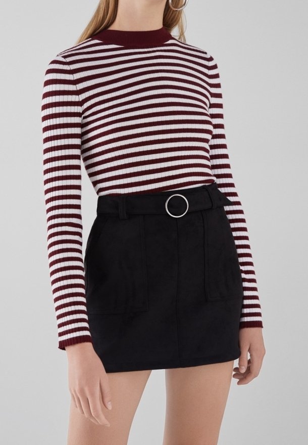 Femme portant un haut à manches longues rayé bordeaux et blanc, rentré dans une jupe noire taille haute avec une ceinture à boucle circulaire.