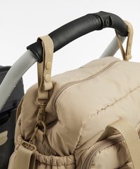 Rucsac căptușit bej atașat cu cleme cu cataramă la mânerul negru al căruciorului sau al căruciorului de cumpărături.