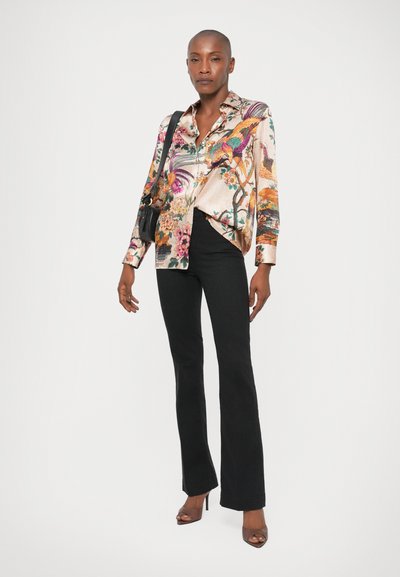 Camisa de satén floral con botones en colores pastel, combinada con pantalones acampanados negros y sandalias de tacón alto marrones. Un bolso de hombro añade funcionalidad.
