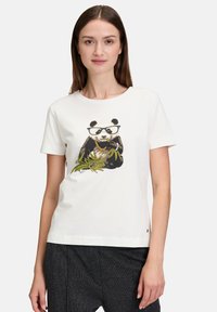 Weißes Baumwoll-T-Shirt mit einem aufgepressten Panda, der Brille und eine goldene Kette trägt, umgeben von grünen Bambusblättern. Kurze Ärmel, rundhalsausschnitt.
