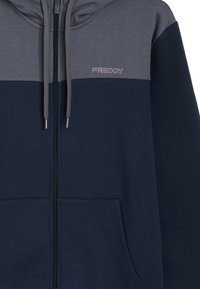 Sudadera con capucha azul marino y gris con cremallera, confeccionada en tejido suave, con gran bolsillo frontal, capucha con cordón y el logo "FREDDY" en el pecho.