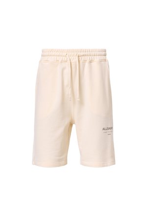 Cream cotton shorts with an elastic waistband and drawstring, featuring side pockets and a small gray logo print on the lower left side.