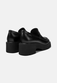 Pareja de mocasines de cuero negro con plataforma y suelas de goma gruesa, punteras redondeadas y etiqueta de marca sutil en la zona del talón.