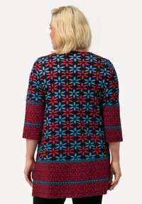 Geprinte tuniek met bloemdesign in rood en blauw op een zwarte achtergrond; heeft driekwart mouwen en contrasterende randen.