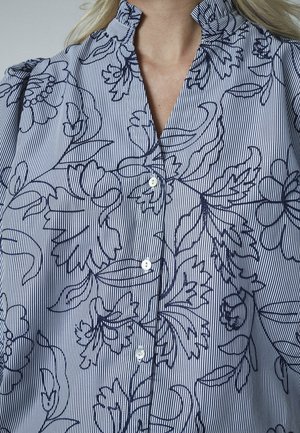 Knapbluse i let stof med blå og hvide striber, der har blomsteromrids, ruffles ved kraven og knapper foran.