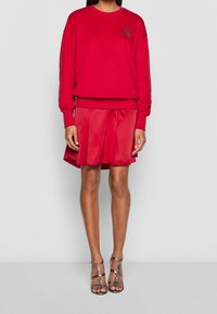 Sudadera roja con bordado "LOVE", combinada con una falda plisada roja. El conjunto presenta un ajuste relajado y una textura suave. Tacones plateados con tiras.