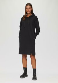 Zwarte hoodie jurk met een relaxte pasvorm, voorzakken, ribgebreide manchetten, zijsplitten aan de onderkant en een verstelbare capuchon met trekkoord.
