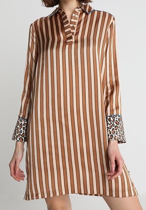 Long-sleeve dress with vertical brown and beige stripes, leopard print cuffs, and a short buttoned collar, worn by a woman.