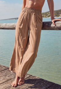 Pantaloni palazzo leggeri a righe in beige con sottili linee blu, dotati di vita elastica e vestibilità comoda, adatti per le giornate calde.