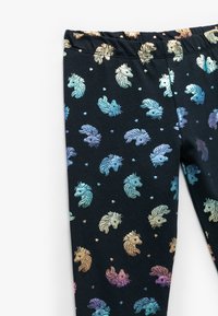 Zwarte leggings met een herhaald patroon van glanzende, iriserende eenhoorn- en visiconen met kleine hartjes, elastische tailleband, gladde textuur.