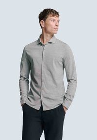 Hellgrau langärmliges Hemd mit Kragen, featuring eine glatte Textur und minimalistisches Design, kombiniert mit dunklen Hosen.