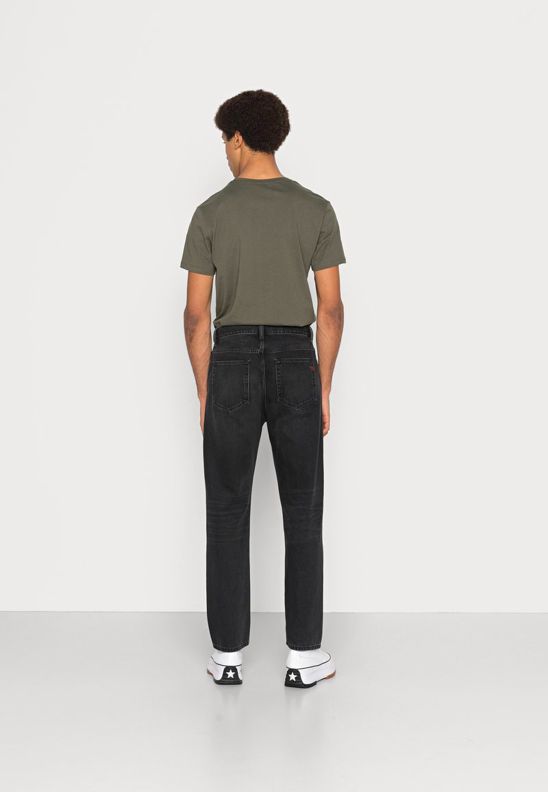 Zwarte jeans met een rechte pasvorm en vijf zakken, gecombineerd met een aansluitend olijfgroen T-shirt. Witte sneakers met zwarte accenten.