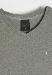 Szara koszulka z dekoltem w serek wykonana z miękkiego materiału; posiada małe, haftowane logo na piersi; metka rozmiaru wskazuje "XL."