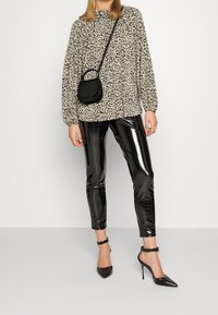 Blusa con stampa leopardata beige e nera, abbinata a leggings neri lucidi. Accessoriata con una piccola borsa a tracolla nera e scarpe con tacco nere.