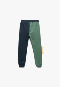 Kinder-Jogginghosen aus einer dunkelblauen und grünen Baumwollmischung. Mit elastischem Bund und einem gelben Stoffdinosaurierschwanz-Detail auf einer Seite.