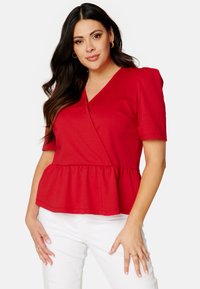 Rode peplum top met korte mouwen, V-hals en gathered taille. Zachte stof met een gladde textuur, gecombineerd met witte broeken.