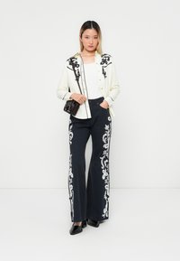 White button-up shirt with black floral embroidery, paired with navy wide-leg pants featuring white floral accents. Black square-toed shoes.