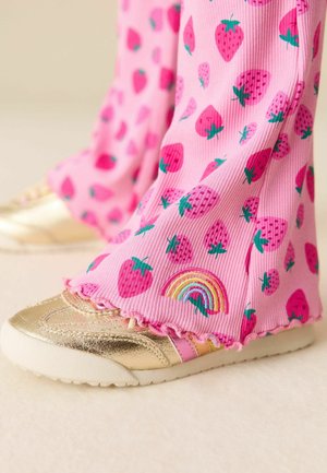 Lyserøde ribbede bukser med jordbærmønstre og en regnbueaccents, kombineret med guldmetalliske sko med en tekstureret overflade.