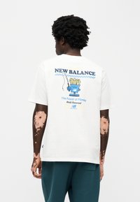 Λευκό βαμβακερό μπλουζάκι με κοντά μανίκια και άνετη εφαρμογή, που απεικονίζει πολύχρωμο γραφικό ενός δοχείου πατάτας τηγανιτής με κείμενο.