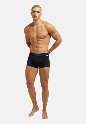 Black fitted boxer shorts with a soft waistband, featuring a logo patch. The model has a muscular build, standing against a neutral background.