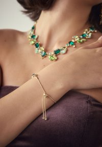 Gold-tone bracelet with adjustable chain, features a smooth centerpiece and two dangling beads. Colorful gemstone necklace with green tones.