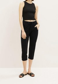Pantalons cropped noirs avec taille élastique et poches latérales, associés à un haut noir ajusté sans manches et des sandales glissantes noires.