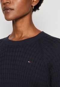 Maglione lavorato a maglia blu navy con motivo testurizzato, scollatura rotonda e logo discreto. Presenta polsini e orlo a coste per un look aderente.